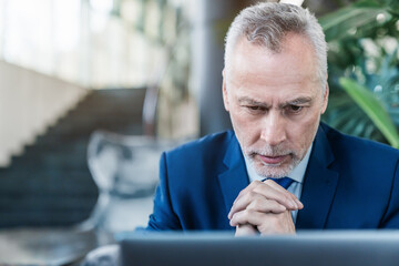 Fototapeta premium Senior businessman boss CEO investor lawyer working on laptop computer while sitting at lobby modern office, analyzes market information statistics. Thoughtful man looking on screen