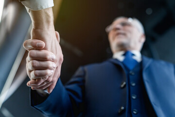 Low angle view of two business people shaking hands while standing indoors. Close up shot of...