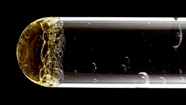 Macro Shot of Different Sized Gold Bubbles in descending in Glass Test Tube on Black Background. Body Care Cosmetics Concept. Essence, Liquid Bubble, Molecule. Slow Motion . High quality 4k footage