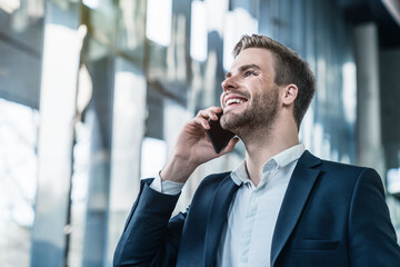 Smiling executive talking on mobile phone in business center hall. Young man businessman entrepreneur investor wearing suit holding telephone making corporate call on cellphone.