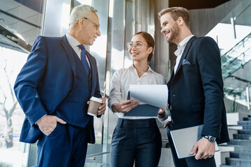 Smiling business people discussing over documents new business plan during a meeting in office lobby. Team of diversity colleagues partners coworkers standing in the hall.