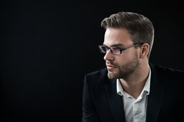 Portrait of young confident guy in eyeglasses over black background with look away. Side view shot...