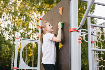 Pre-teen girl scaling a climbing wall in a summer park. Healthy active lifestyle concept, sports...