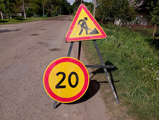 Road surface repair is underway on a rural road on which there are two signs, one emergency road repair sign and a speed limit sign up to 20 km/h. The topic of road repair.