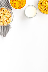 Various corn cereals in bowls and milk on white background top view copyspace