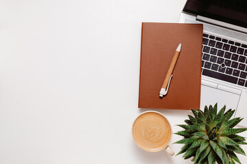 Workspace background with copy space. Notepad on laptop, home plant and cup of coffee on white...