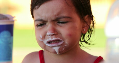 Upset little girl covered with yogurt in mouth nodding no