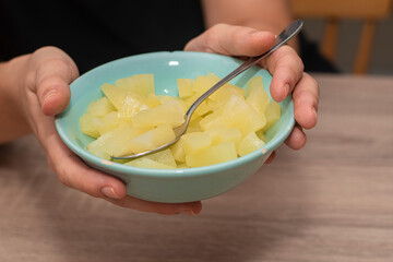 Serving Bowl of Diced Pineapple. Close-up view of a person's hands holding a bowl of freshly diced pineapple pieces, ready to eat with a spoon