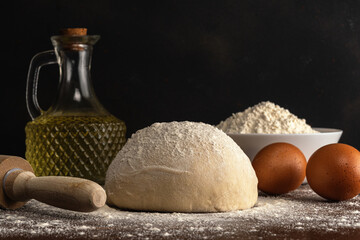 Fresh raw dough for bread or pizza with eggs and oil on a dark wooden table.