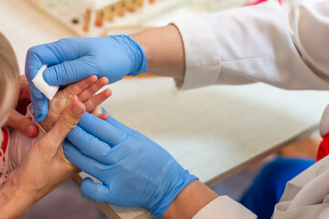 the mother holds the child's hand, and the nurse wipes the finger with a disinfecting swab, sterilizing it before taking blood