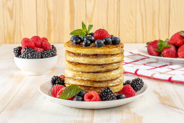 Delicious pancakes with fresh berries on white wooden table. Food concept.