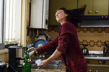 An adult latin woman is washing dishes in a kitchen