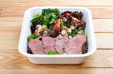 Salad with roast beef sous-vide. Healthy food. Takeaway food.  On a wooden background.