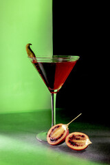 Martini glass with a cut tamarillo piece with a green and black background