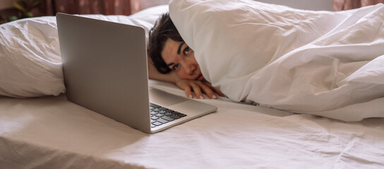 Lady working remotely while lying in bed talking on a video call.