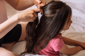 Mom braids her daughter's hair while sitting in bed.