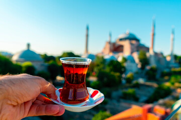 A man drinks Turkish tea opposite the Hagia Sophia Mosque. The man drinks his tea while admiring...