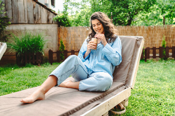 One young caucasian woman is relaxing on easy bed while drinking cold coffee in her backyard	