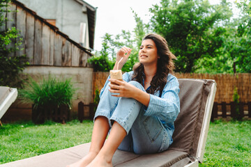 Fototapeta premium One young caucasian woman is relaxing on easy bed while drinking cold coffee in her backyard 