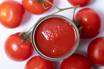 Tomato sauce in tin can, with fresh tomatoes around, white background, top view,