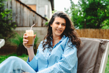 One young caucasian woman is relaxing on easy bed while drinking cold coffee in her backyard	