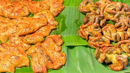 Marinated pork and grilled intestines are neatly arranged on banana leaves at street food market....