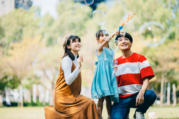 An Asian family of three heads to the park for a picnic, indulging in games and blowing bubbles...