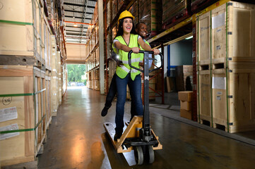 Happy Caucasian woman and African man warehouse workers having fun together playing with trolley in...