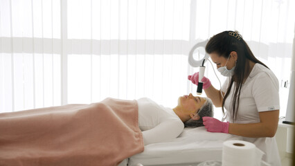 A young woman lies on a couch during a facial treatment. Hardware facial procedure. Side view of a...