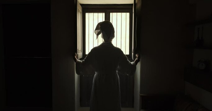 Woman in robe room of an old hotel looks out window and closes it. young woman stands in room by window and closes shutters. Girl close curtains. Young female approaches window and closes curtains