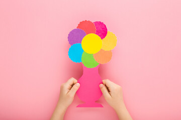 Baby girl hands holding and showing beautiful flower head and vase shape from colorful paper on...