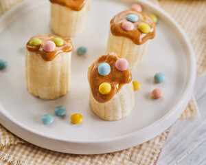 Banana healthy snacks with peanut butter, colorful sprinkles on a light wooden table. Close Up. Breakfat or brunch for kids. Selective focus.