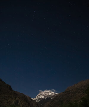 Minimalistic night landscape of the Greater Hansa mountain peak at night against the backdrop of a clear starry sky, a cold mountain with snow and glaciers in the evening
