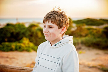 Happy cheerful teenager standing on beach at sunset. happy preteen boy smiling at the camera. Kid on family vacation at the sea.