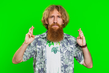 Caucasian man crossed fingers looking at camera asking for good luck news, wishing good exam results, dreaming about win victory in lottery jackpot. Redhead guy isolated on green chroma key background