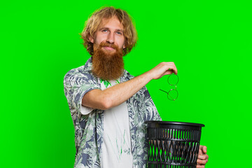 Redhead man taking off throwing out glasses into bin after medical vision laser treatment therapy surgery looking smiling at camera, heal, cure. Handsome guy isolated on green chroma key background