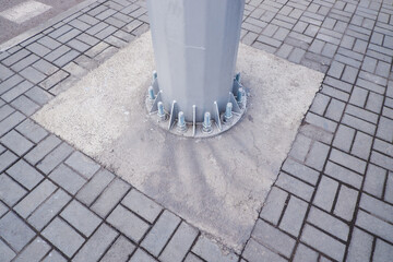 A pole with a lot of screws on it is sitting on a brick sidewalk