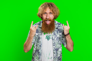 Overjoyed happy young caucasian man showing rock n roll gesture by hands, cool sign, shouting yeah with crazy expression dancing, rejoicing victory, win, success. Guy on green chroma key background