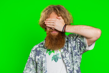 Dont want to look at this, awful. Afraid shocked caucasian man closing eyes with hand showing stop gesture, confused shy scared reject to watch. Redhead guy isolated on green chroma key background