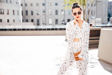 Young beautiful confident woman in trendy summer white costume clothes. Sexy carefree model posing in the street at sunset. Positive brunette female. Cheerful and happy. red lips