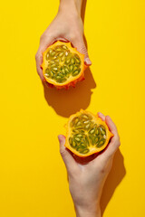 Two half of kiwano fruit in hands on yellow background, top view