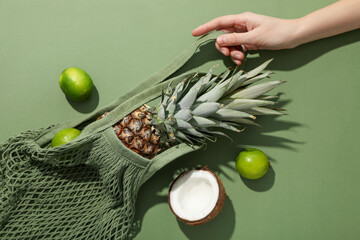 Bag with tropical fruits in hand on green background, top view