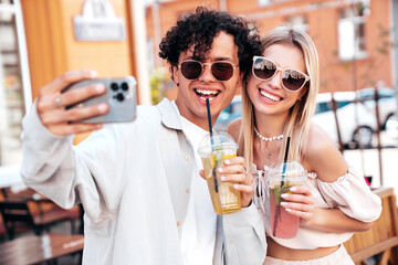 Young smiling beautiful woman and her handsome boyfriend in casual summer clothes. Happy cheerful family. Female having fun. Couple posing in street. Holding and drinking cocktail drink in plastic cup