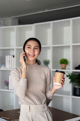 Successful businesswoman speaking by smartphone and smiling happily while standing in office