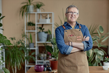 Waist up portrait of smiling senior man wearing apron posing with green plants at home and enjoying gardening, copy space