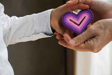 Close-up of the hand of a Caucasian boy dressed in a white shirt giving a purple pink heart made of...