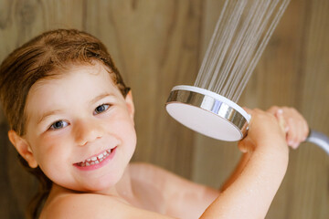 Little toddler girl taking bath shower. Happy healthy preschool child playing with shower head and...