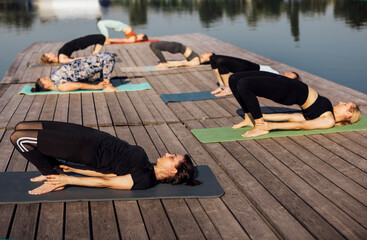 Yoga class with an instructor at the city pier. A group of young multiracial women lie in a...