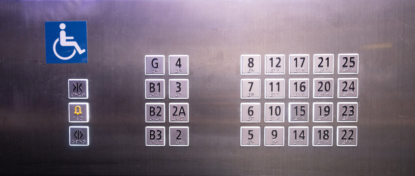 A sign for an elevator with a blue wheelchair symbol. The buttons are numbered from 1 to 25 with Braille alphabet for invisible people.