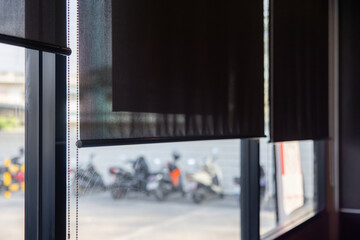A window with a pair of roller shades and a motorcycle parked outside. black blind curtain.